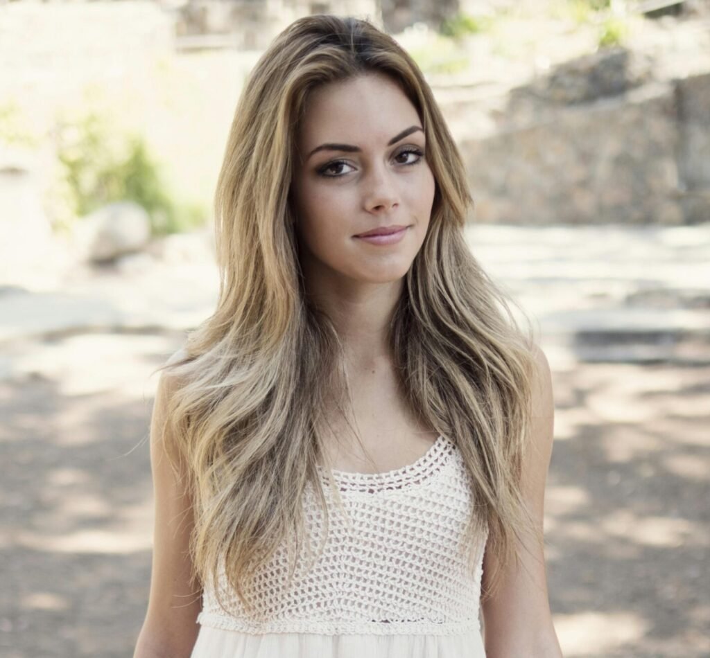 Portrait of a young woman in a white dress sitting outdoors on a sunny day.